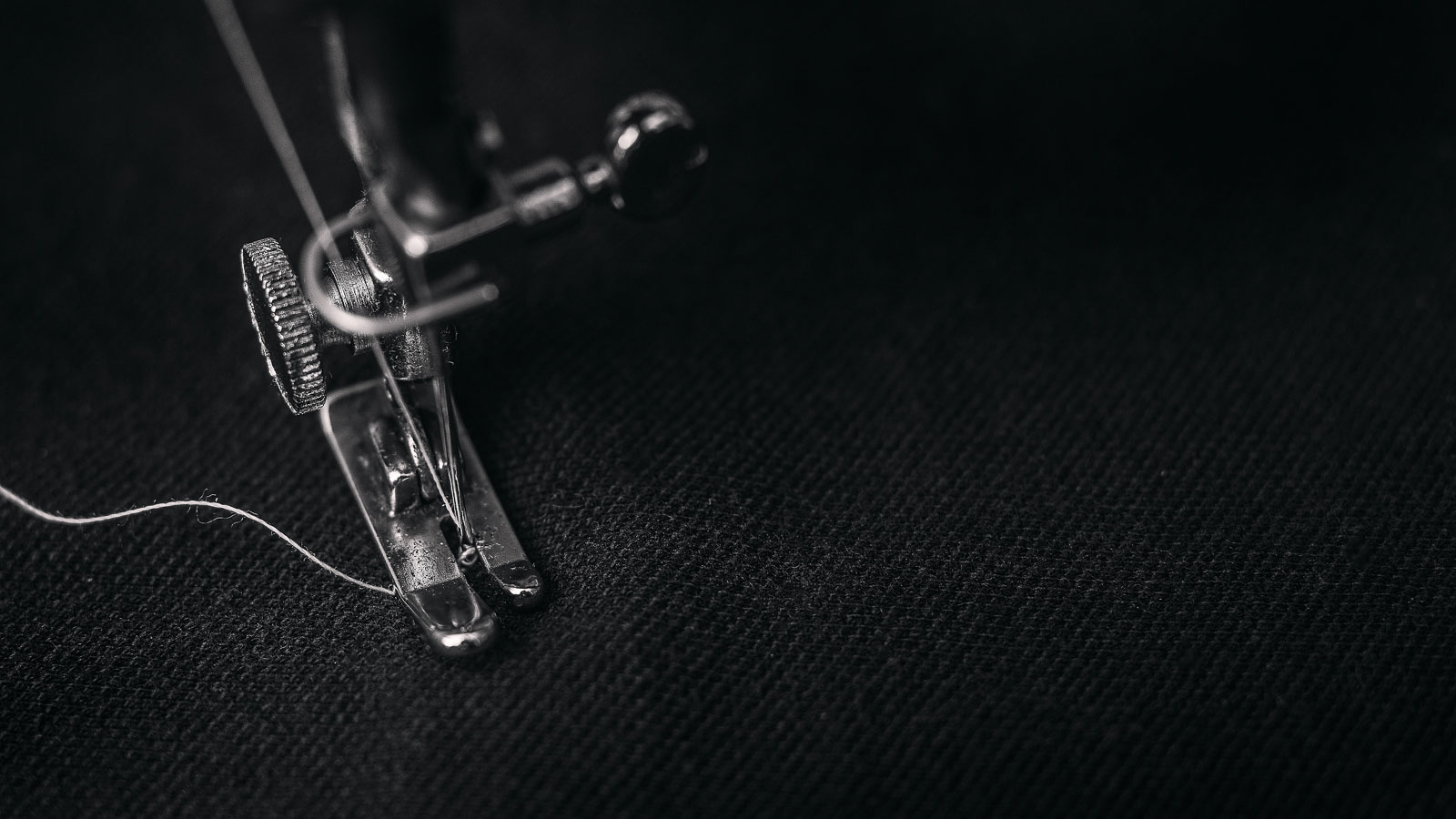 Narrow straight stitch sewing machine foot, needle and white thread on black fabric.